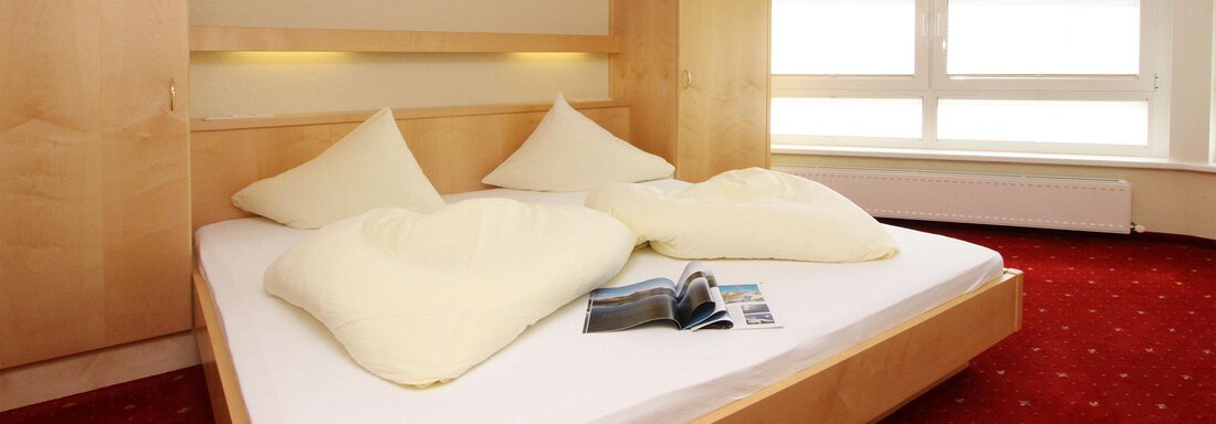 A cozy bedroom with a large double bed and two pillows. Large windows let in a lot of light and the floor is covered with a red carpet. - Hotelappart Peter - Sölden
