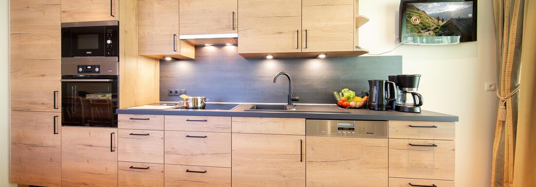 A modern kitchen with wooden cabinets and sleek appliances. On the countertop are fruits and a coffee machine. - Hotelappart Peter - Sölden