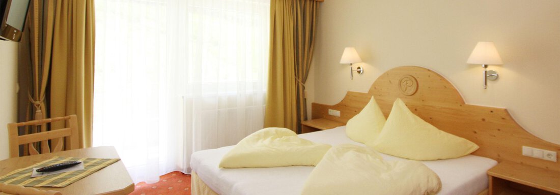 A cozy bedroom with a large double bed and bright pillows. The room is friendly and bright with a small table and chairs. - Hotelappart Peter - Sölden