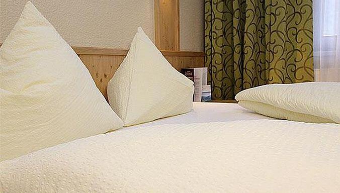 A cozy bed with fresh, white pillows and blankets. In the background, a green curtain can be seen. - Hotelappart Peter - Sölden