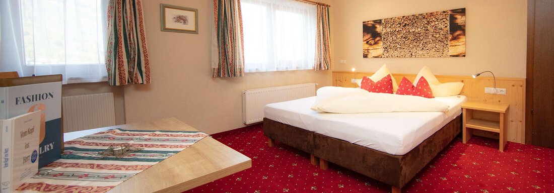 A cozy bedroom with a large bed and red carpet. Bright windows create a friendly atmosphere. - Hotelappart Peter - Sölden