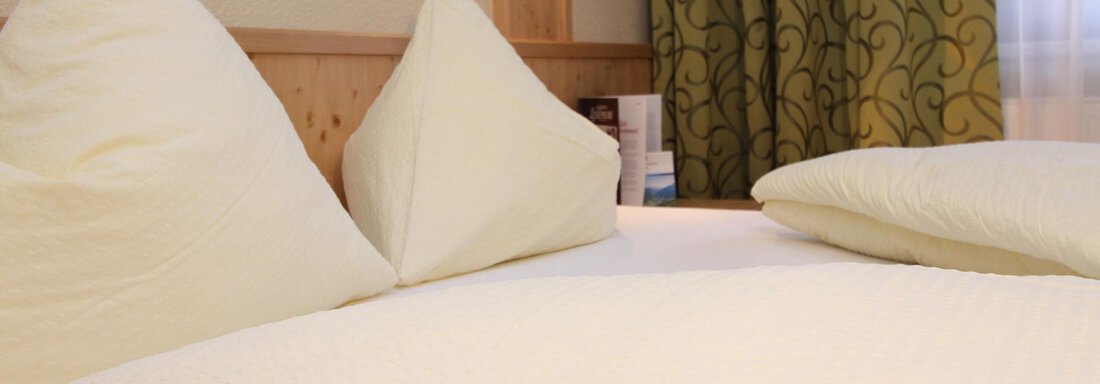 A cozy bed with white pillows and a light duvet. In the background, green curtains are visible. - Hotelappart Peter - Sölden