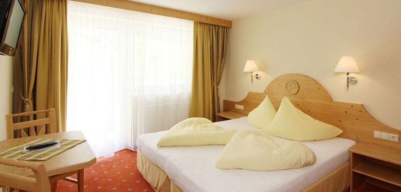 A cozy hotel room with a large double bed and yellow pillows. The room has bright walls and plenty of natural light. - Hotelappart Peter - Sölden