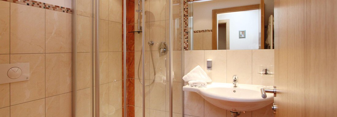A modern bathroom with a shower cabin and a sink. The walls are light tiled and there are wooden details. - Hotelappart Peter - Sölden