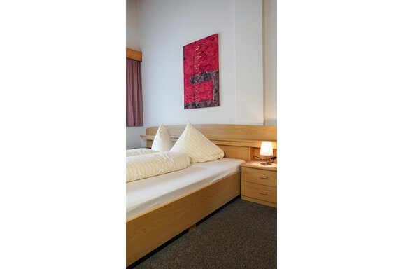 Ein gemütliches Schlafzimmer mit einem Doppelbett und modernen Kissen. An der Wand hängt ein farbenfrohes Kunstwerk und ein Nachttisch mit einer Lampe steht daneben. - La Luna - Sölden