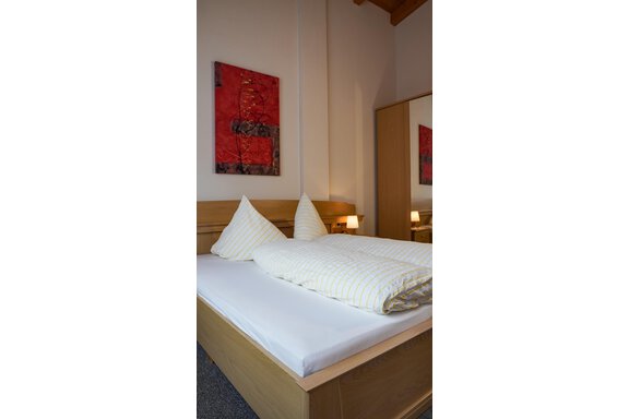 Ein modernes Schlafzimmer mit einem Doppelbett und hellen Kissen. An der Wand hängt ein rotes Kunstwerk, und neben dem Bett stehen zwei Nachttische mit Lampen. - La Luna - Sölden