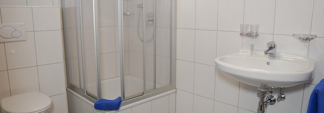 Ein modernes Badezimmer mit einer gläsernen Dusche, einem Waschbecken und einer Toilette. Die Wände sind gefliest, und es liegen blaue Handtücher bereit. - La Luna - Sölden