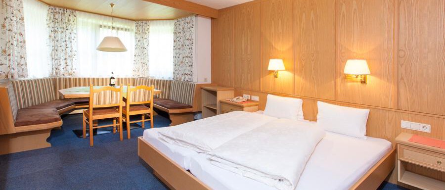 Schlafzimmer A cozy hotel room with a double bed and wooden furniture. In the background, there is a dining area with a table and chairs. - Landhaus Falkner - Sölden