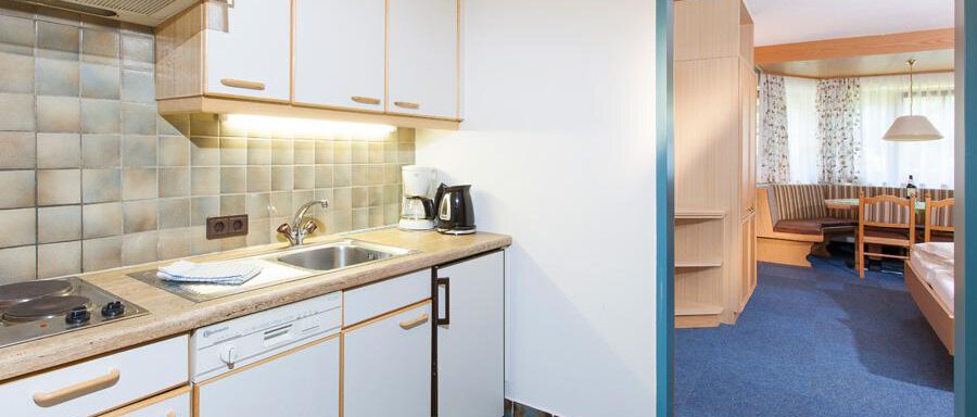 A modern kitchen with wooden cabinets and a sink. In the background, there is a living area with cozy furniture. - Landhaus Falkner - Sölden