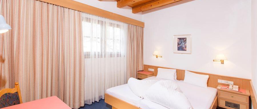 Schlafzimmer A cozy bedroom with a wooden ceiling and large windows. A bed with white pillows and a table can also be seen. - Landhaus Falkner - Sölden
