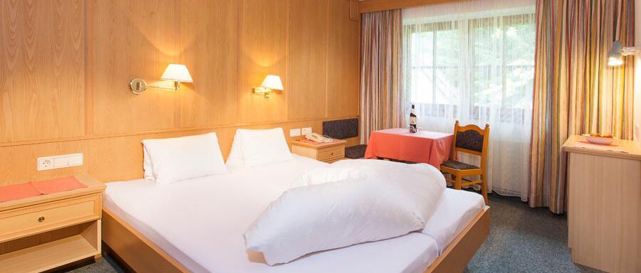 A cozy hotel room with a double bed and wooden paneling. The windows let in plenty of light, and the room is simply but invitingly furnished. - Landhaus Falkner - Sölden
