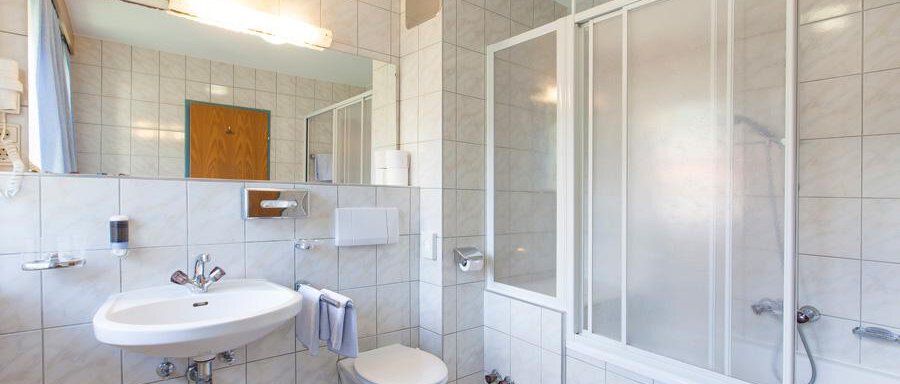 Badezimmer A modern bathroom with tiles and a large mirror. There is a shower, a bathtub, and a sink. - Landhaus Falkner - Sölden