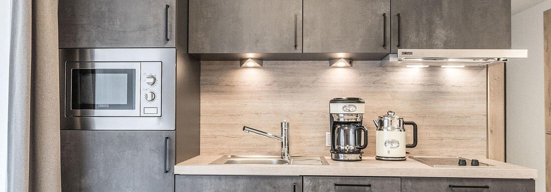 Wohnküche A modern kitchen with dark cabinets and a light countertop. There is a microwave, a coffee maker, and a kettle. - Landhaus Falkner - Sölden