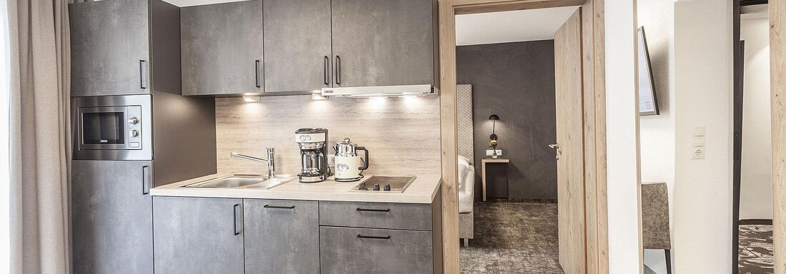 A modern kitchen with dark cabinets and integrated appliances. The space is bright and inviting, with access to another room. - Landhaus Falkner - Sölden