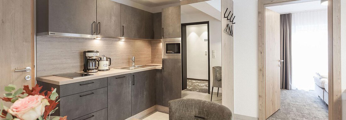 Wohnküche A modern kitchen with wooden cabinets and a dining table. The room is bright and inviting, with access to another room. - Landhaus Falkner - Sölden