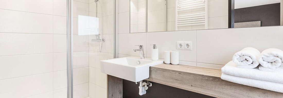 A modern bathroom with a walk-in shower and a sink on a wooden shelf. Fresh towels and a large mirror wall create a bright atmosphere. - Landhaus Falkner - Sölden