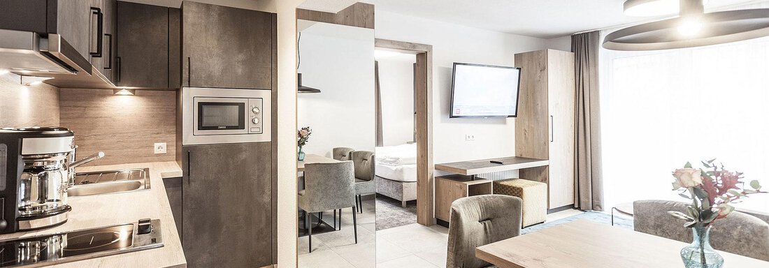 A modern kitchen unit with elegant furniture and a dining table. The room is bright and welcoming, with two windows that let in natural light. - Landhaus Falkner - Sölden