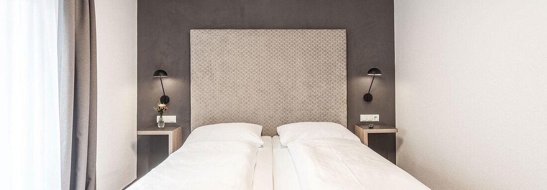 A modern bedroom with two single beds and an elegant wall design. Next to the beds are two nightstands with lamps on each side. - Landhaus Falkner - Sölden