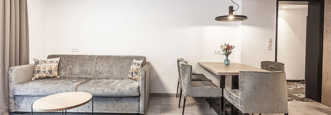 A modern living room with a gray sofa and a round coffee table. The dining area includes a table with chairs and is illuminated by a modern lamp. - Landhaus Falkner - Sölden