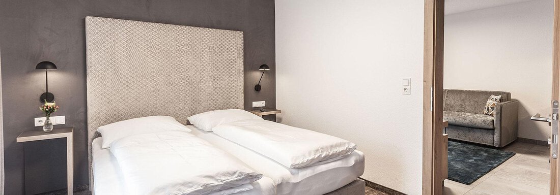 A modern bedroom with two single beds and stylish decor. The room is bright and inviting, with a door to an adjacent living area. - Landhaus Falkner - Sölden