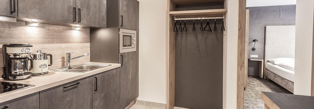 A modern kitchen with gray cabinets and a small countertop. In the background, a sleeping area is visible. - Landhaus Falkner - Sölden
