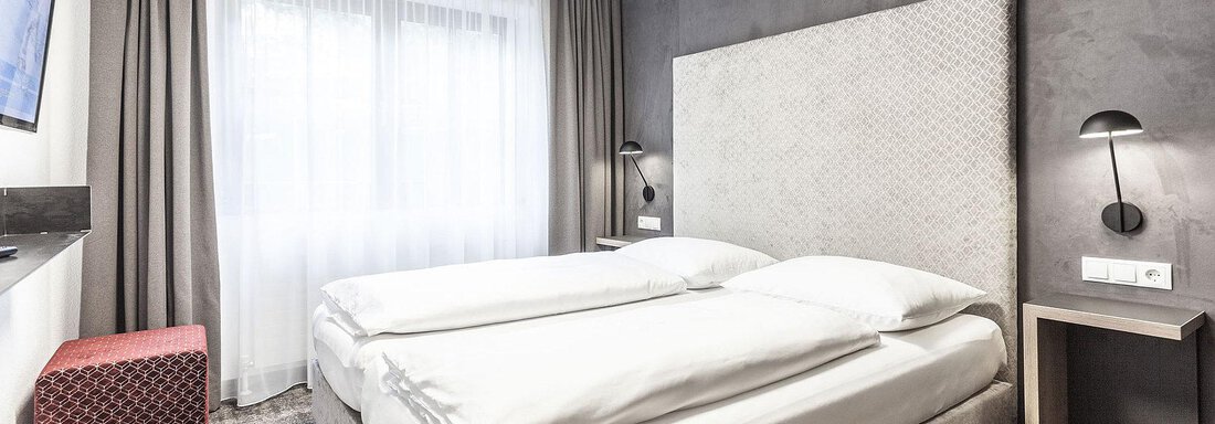 A modern hotel room with a double bed and a large window. The walls are painted in neutral colors, and there is contemporary furniture. - Landhaus Falkner - Sölden