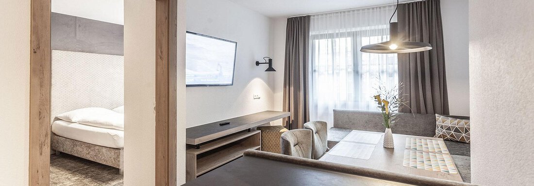 A modern living room with a dining table and a cozy seating area. The room is brightly lit and offers a view of the bedroom. - Landhaus Falkner - Sölden