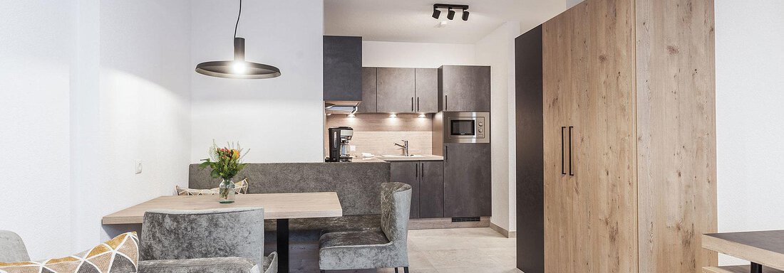 A modern kitchen with a wooden dining area and gray chairs. The space is bright and well-furnished with simple, elegant furniture. - Landhaus Falkner - Sölden