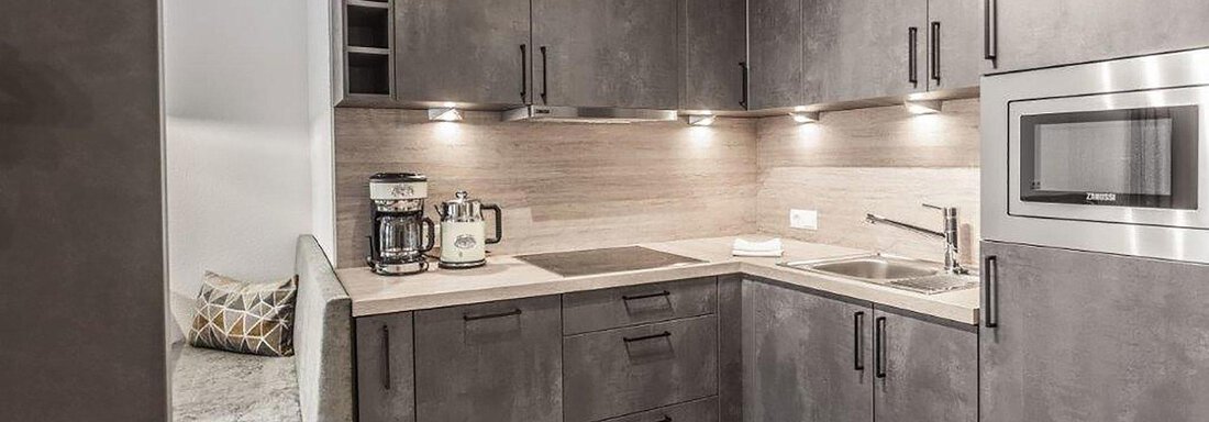 A modern kitchen with dark cabinets and bright work surfaces. It is well-equipped and has a cozy seating area. - Landhaus Falkner - Sölden