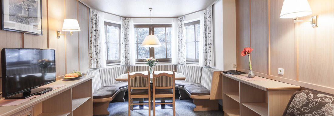 A cozy living arrangement with a dining table and chairs. The walls are clad with wooden panels and there are large windows that let in a lot of light. - Landhaus Falkner - Sölden
