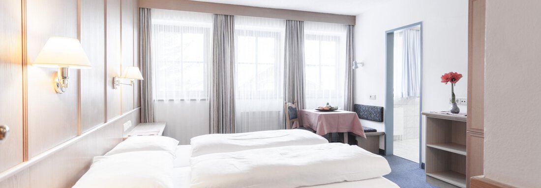 A cozy hotel room with two single beds and neutral decor. Daylight streams through the windows, creating an inviting atmosphere. - Landhaus Falkner - Sölden