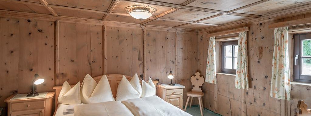 A cozy bedroom with wooden walls and a double bed. The windows are decorated with curtains, and there are bedside tables with lamps. - Landhaus Peater's Hoamat - Sölden