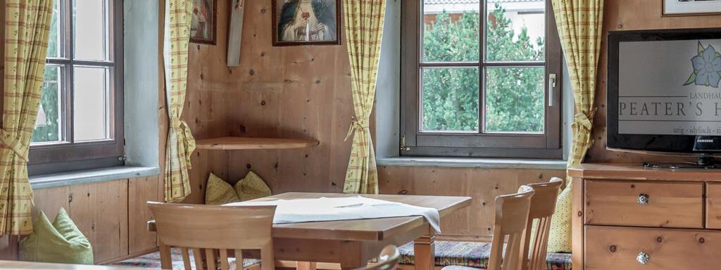 A cozy room with wooden walls and a table. Large windows let in plenty of light, and the furnishings are rustic with classic details. - Landhaus Peater's Hoamat - Sölden