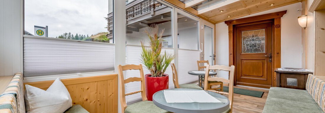 250821_104344 A cozy interior with wooden furniture and large windows. A round table stands between comfortable benches and plants. - Lyns Home - Sölden