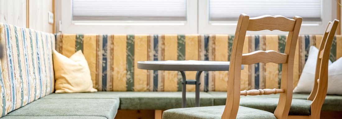 A cozy room with a bench and a round table. The walls are bright and there are large windows that let in daylight. - Lyns Home - Sölden