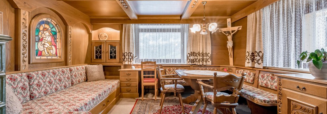 A cozy room with wood-paneled walls and an inviting seating area. A table with chairs stands in the center, surrounded by traditional decor and windows with curtains. - Lyns Home - Sölden