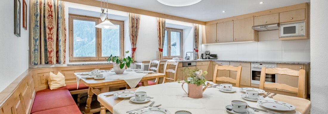 An inviting dining room with a large table, beautifully set with dishes. The walls are bright and the windows let in plenty of daylight. - Lyns Home - Sölden
