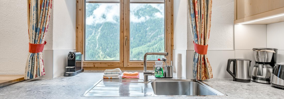 A modern kitchen with wooden cabinets and a stone countertop. Through the window, you can see the beautiful mountains and nature. - Lyns Home - Sölden