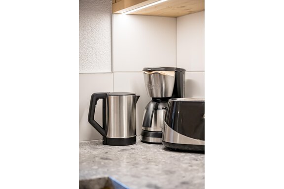 A modern kitchen corner with stainless steel kitchen appliances. On display are a coffee machine, a kettle, and a toaster on a gray countertop. - Lyns Home - Sölden
