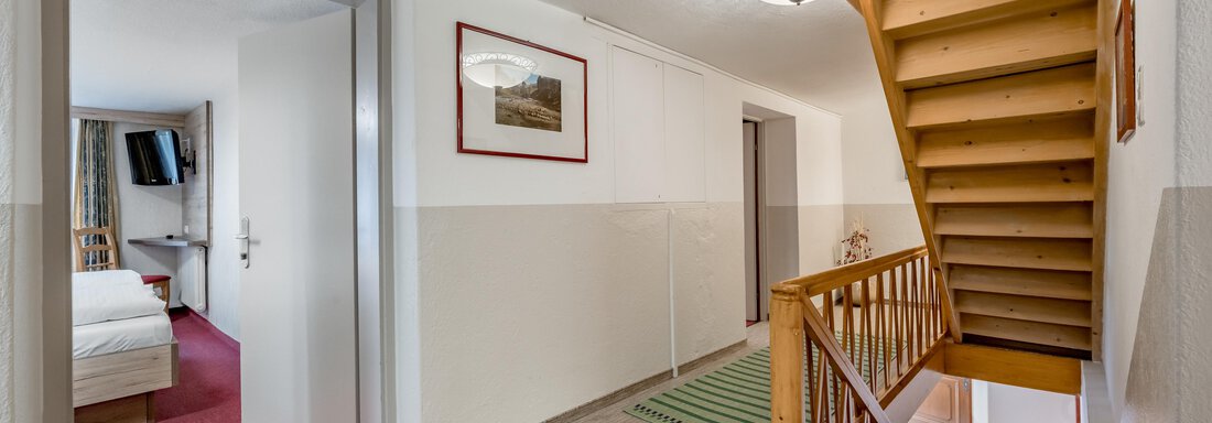 A bright hallway with a staircase and two doors. A picture hangs on the wall and a ceiling lamp provides lighting. - Lyns Home - Sölden