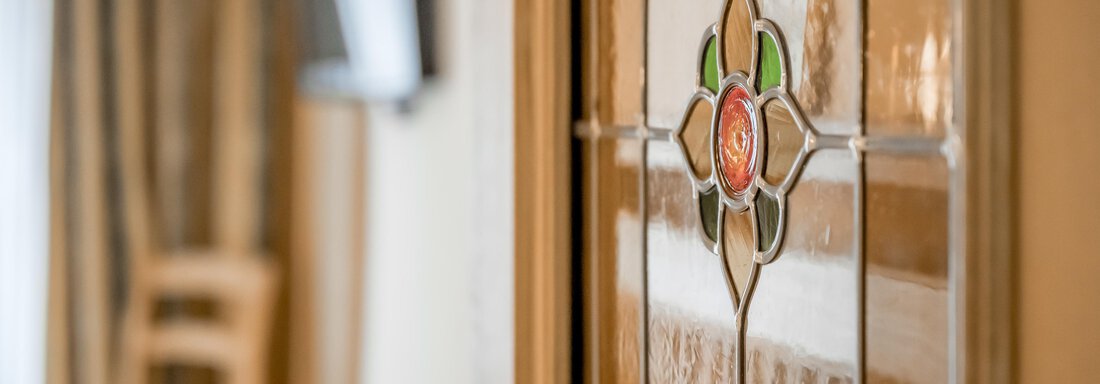A beautiful glass door with a colorful pattern. In the background, there is a room with a television and a chair. - Lyns Home - Sölden