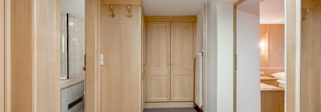 A bright hall with wood paneling and carpet flooring. In the background, various doors can be seen leading to other rooms. - Lyns Home - Sölden