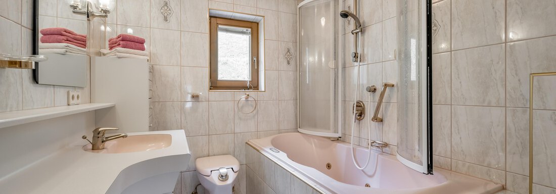 A modern bathroom with a bathtub and a separate shower. The walls are equipped with light tiles and there is a large window opening. - Lyns Home - Sölden