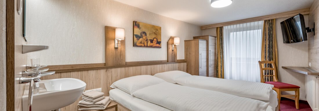 A cozy hotel room with two beds, a modern television, and a sink. The walls are light, and there is a beautiful view through the window. - Lyns Home - Sölden