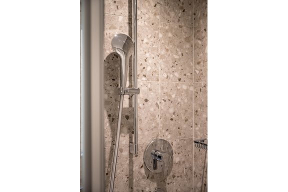 A modern shower with a chrome showerhead and gray tiles. The walls are designed with a textured tile in light shades. - Lyns Home - Sölden