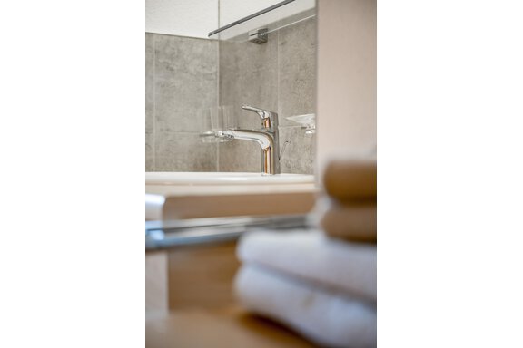 A modern bathroom with a stylish faucet and grey tiles. Rolled towels are visible in the foreground. - Lyns Home - Sölden