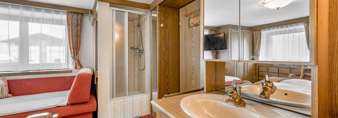 A bedroom with a sink, a mirror, and a shower. The decor is simple and functional, featuring a red sofa and plenty of natural light. - Lyns Home - Sölden