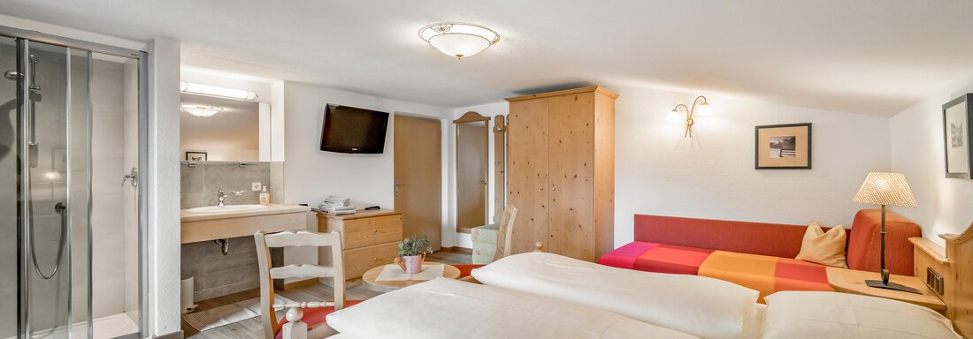 A cozy room with two beds and a red sofa. There is a modern bathroom and warm wooden furniture. - Lyns Home - Sölden