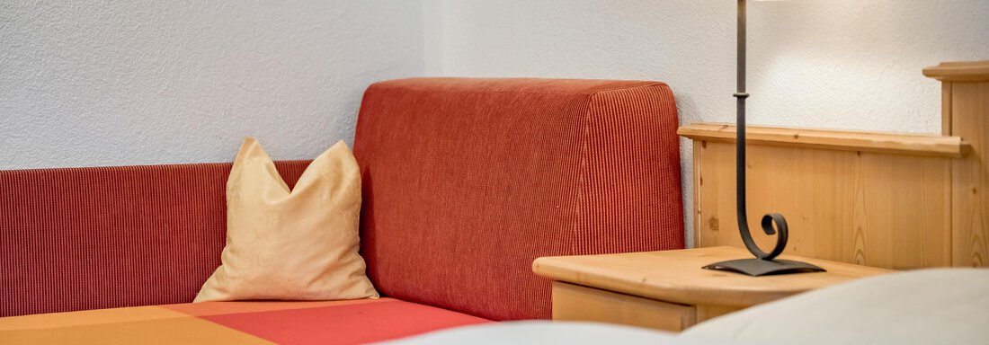 A cozy living area with a red couch and a beige cushion. Next to the couch stands a lamp on a wooden tray. - Lyns Home - Sölden