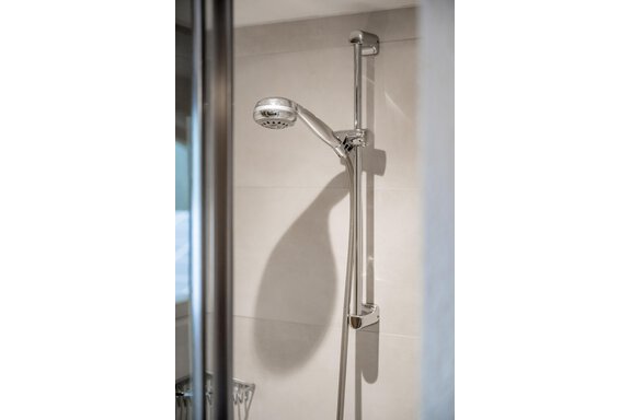 A modern shower with a simple, chrome-handled showerhead. The walls are bright and designed in a minimalist style. - Lyns Home - Sölden